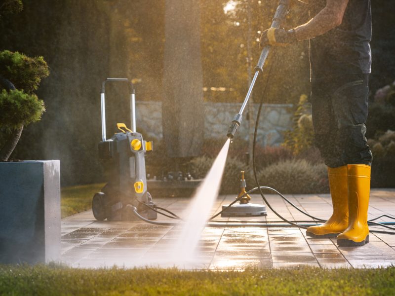 A Person Power Washing a Patio With a Pressure Washer in a Sunny Outdoor Setting